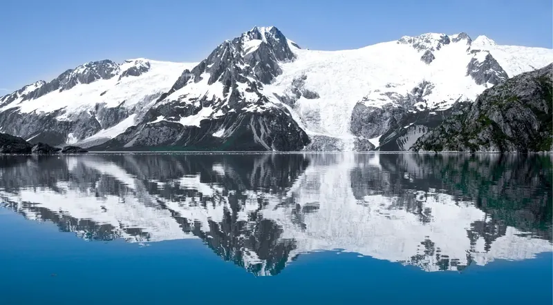 Snow-capped peaks mirrored in calm fjord water in Kenai Fjords National Park, reached on a day trip from Anchorage, Alaska