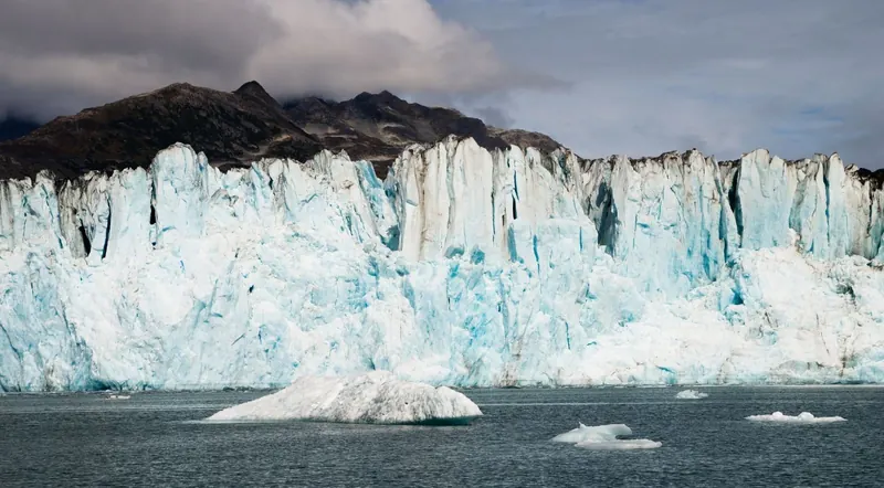 Blue ice cliff of a calving tidewater glacier with icebergs floating in the water, Kenai Fjords National Park