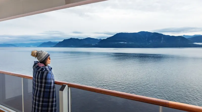 Guest in a waterproof jacket on the open deck of a Kenai Fjords cruise boat watching the fjord