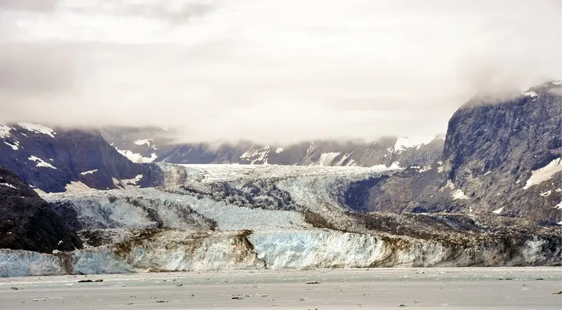 A tidewater glacier terminus under low cloud at the head of a bay in Kenai Fjords National Park, Alaska.